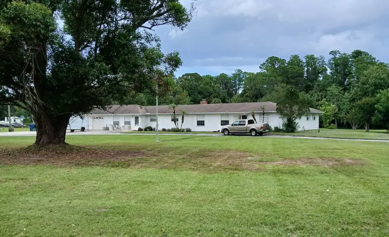 Wide mowed lawn under a large shade tree in front of a long single story home