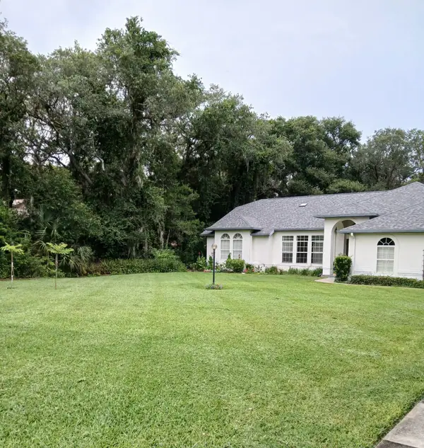 Even green lawn in front of a white home with oaks behind