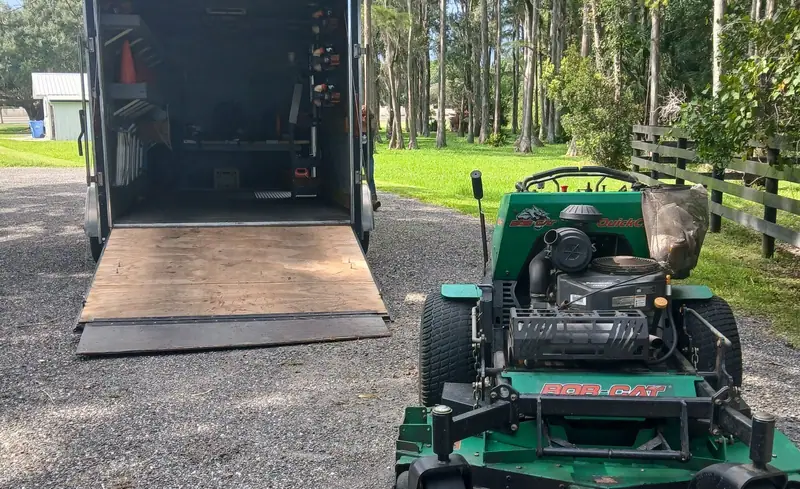 Stand-on mower beside an open enclosed trailer